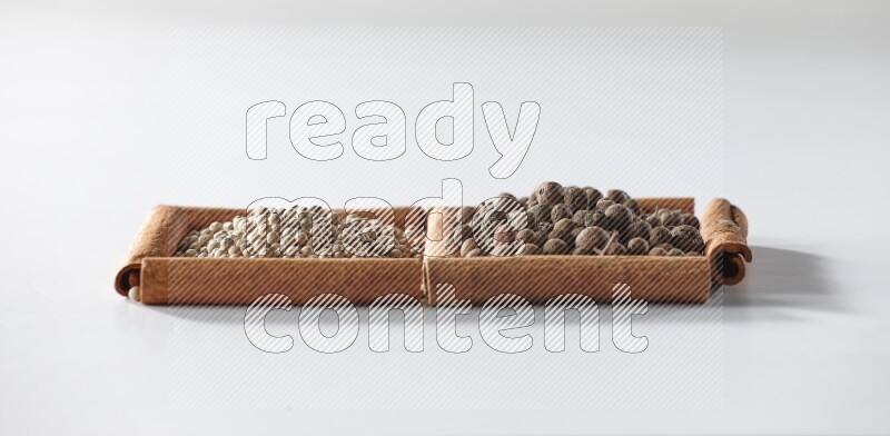 مربعان من أعواد القرفة ممتلئان بحبوب الفلفل الأبيض وحبوب الفلفل الحلو علي خلفية بيضاء