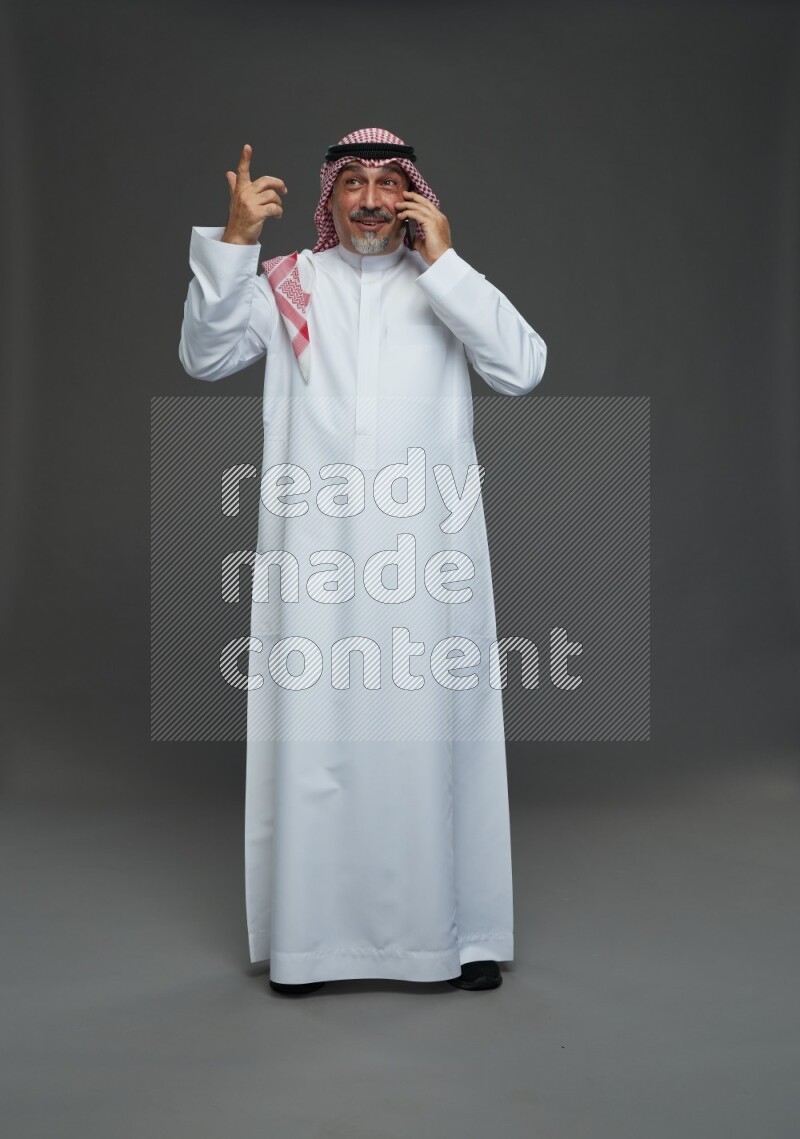 Saudi man with shomag Standing talking on phone on gray background