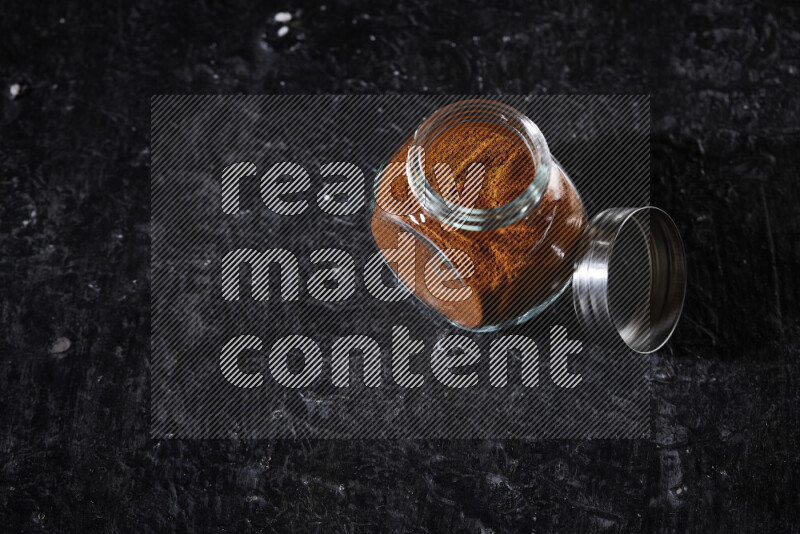 A glass jar full of ground paprika powder on black background