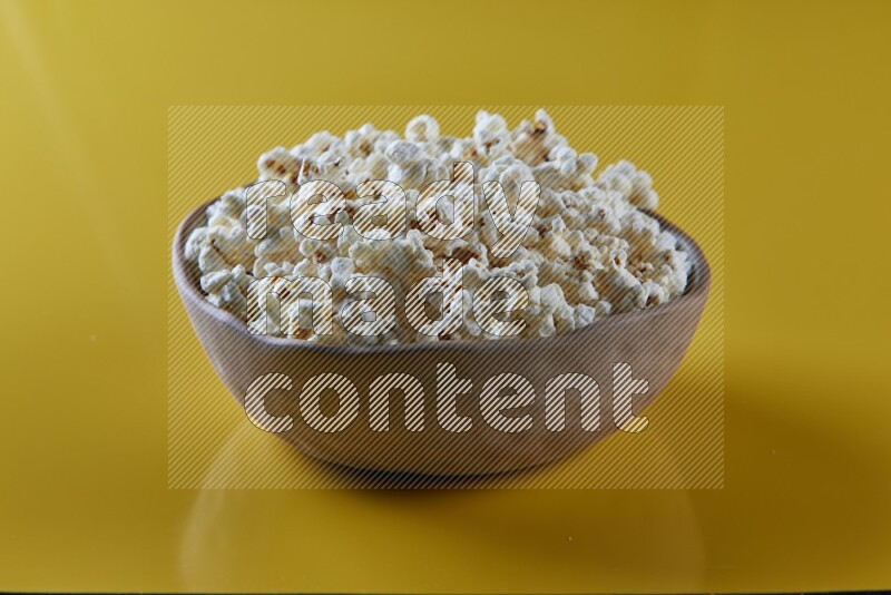 A brown pottery bowl full of popcorn on a yellow background in different angles