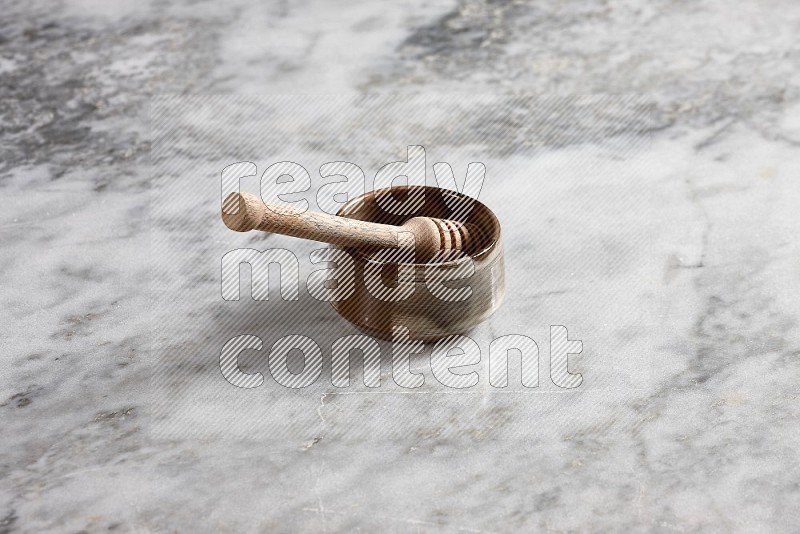 Brown Pottery bowl with wooden honey handle in it, on grey marble flooring, 45 degree angle