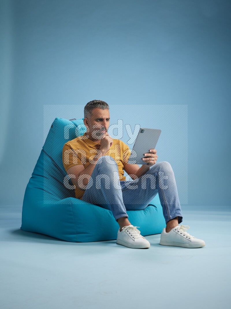 A man sitting on a blue beanbag and working on tablet