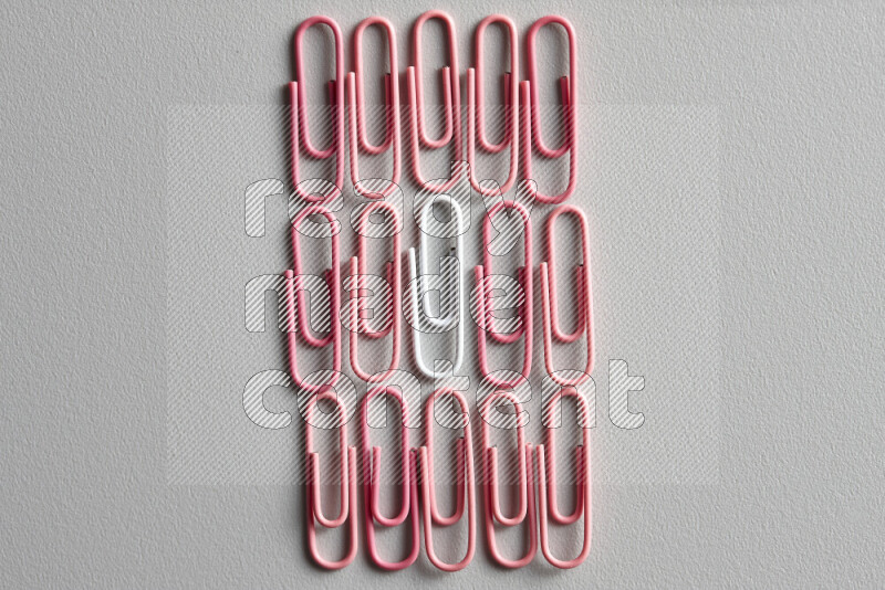 A white paperclip surrounded by bunch of pink paperclips on grey background