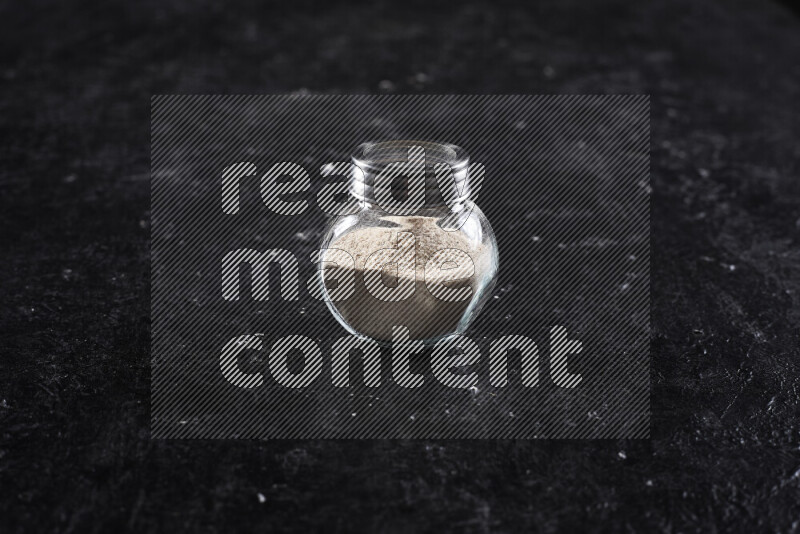 A glass jar full of onion powder on black background