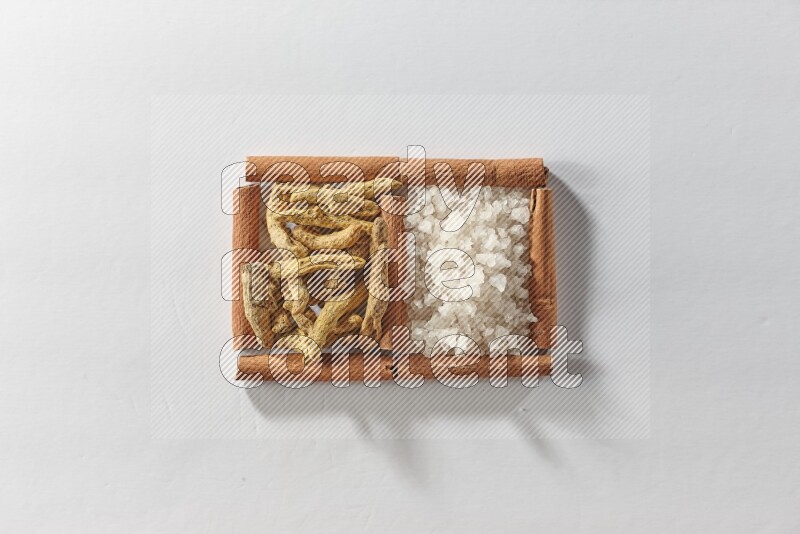 2 squares of cinnamon sticks full of turmeric fingers and white salt on white flooring