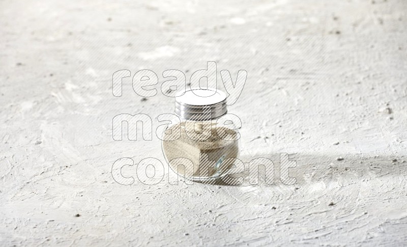 Herbal Glass jar full of white pepper powder on textured white flooring