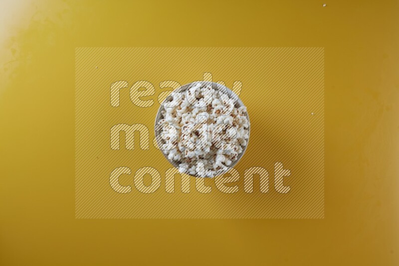 A white pottery bowl full of popcorn on a yellow background in different angles