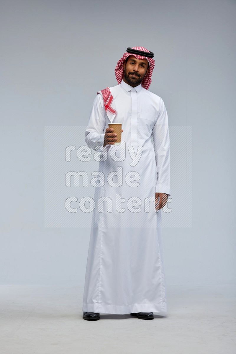 Saudi man Wearing Thob and shomag standing holding paper cup on Gray background