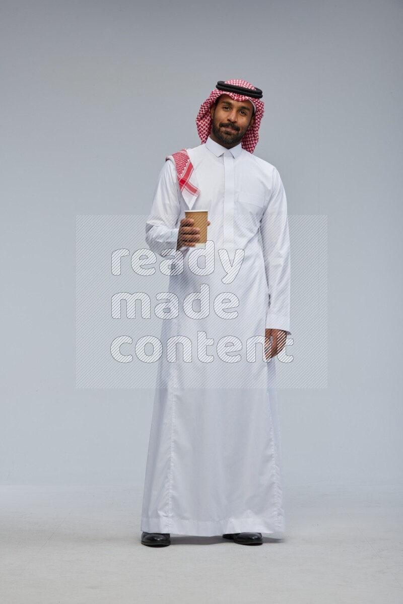 Saudi man Wearing Thob and shomag standing holding paper cup on Gray background