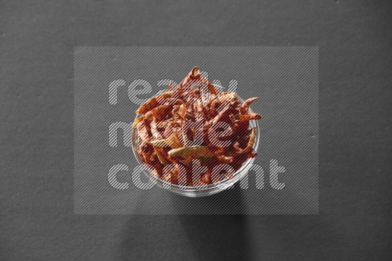 A glass bowl full of dried red chili peppers on black flooring