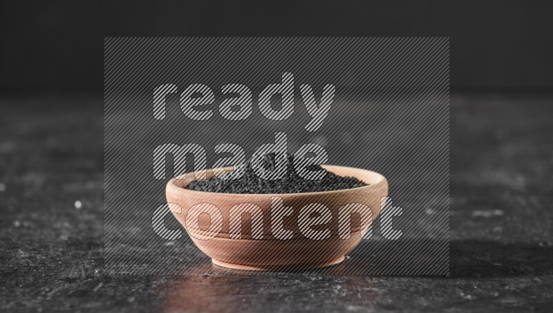 A wooden bowl full of black seeds on a textured black flooring