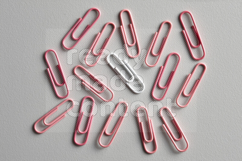 A white paperclip surrounded by bunch of pink paperclips on grey background