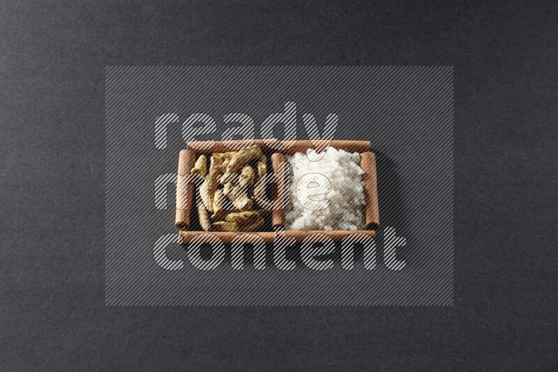 2 squares of cinnamon sticks full of white salt and turmeric fingers on black flooring