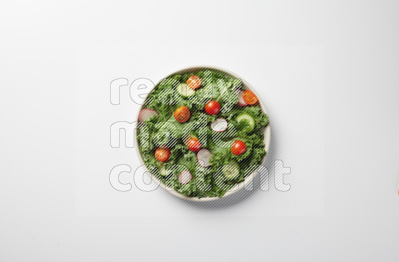 A bowl of fresh vegetables salad with kale leaves, cherry tomatoes, sliced radishes and sliced cucumber on a white background