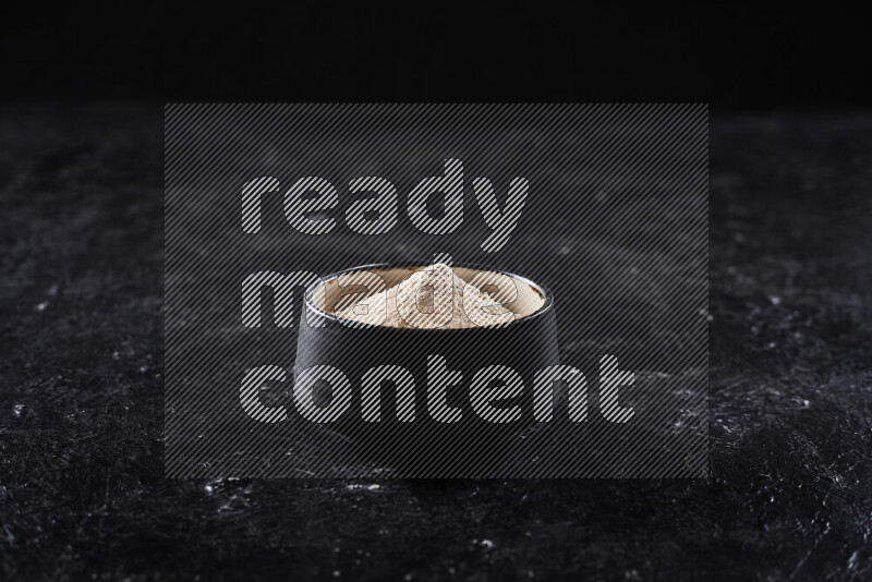 وعاء فخاري اسود ممتلئ ببودرة البصل علي خلفية سوداء