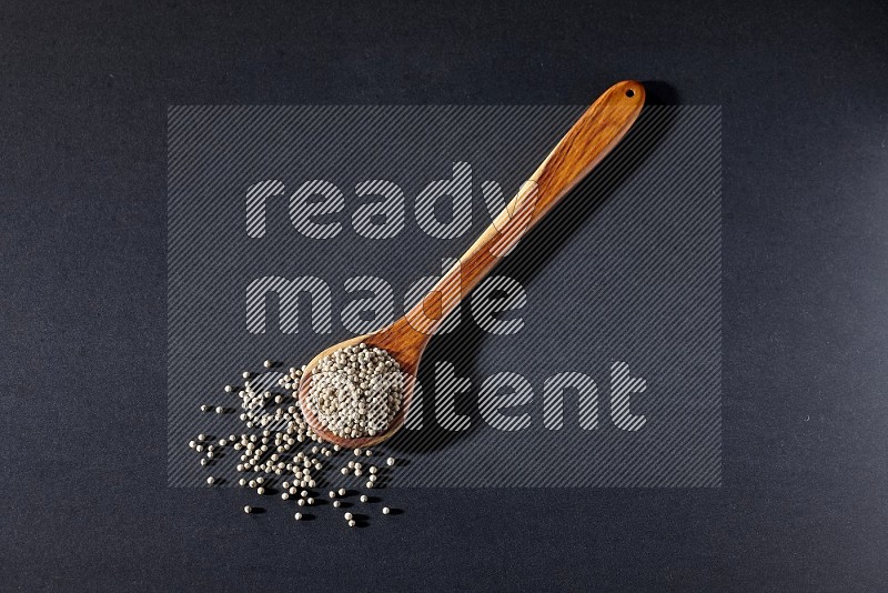 A wooden ladle full of white pepper beads on black flooring
