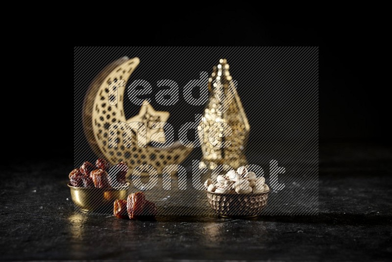 Dates in a metal bowl with pistachios beside golden lanterns in a dark setup