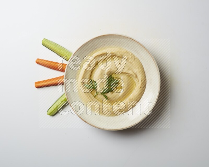Hummus in a pottry plate garnished with parsley on a white back ground