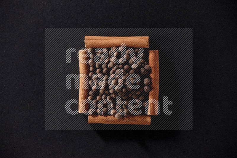A single square of cinnamon sticks full of allspice on black flooring