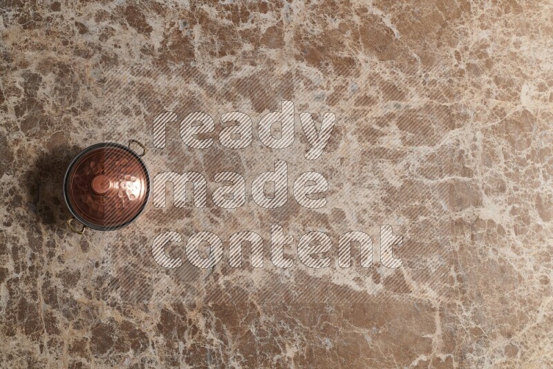 A small copper pot on beige marble background