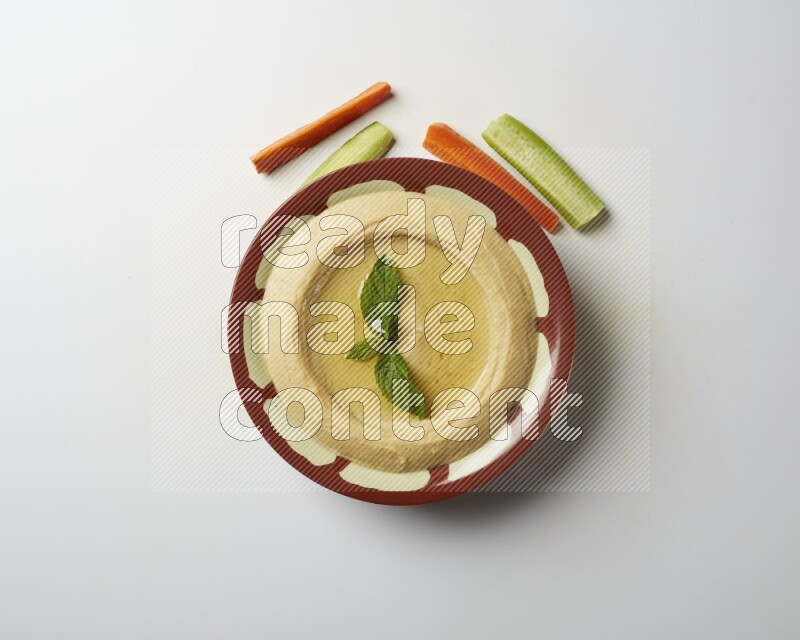 Hummus in a traditional plate garnished with mint on a white background