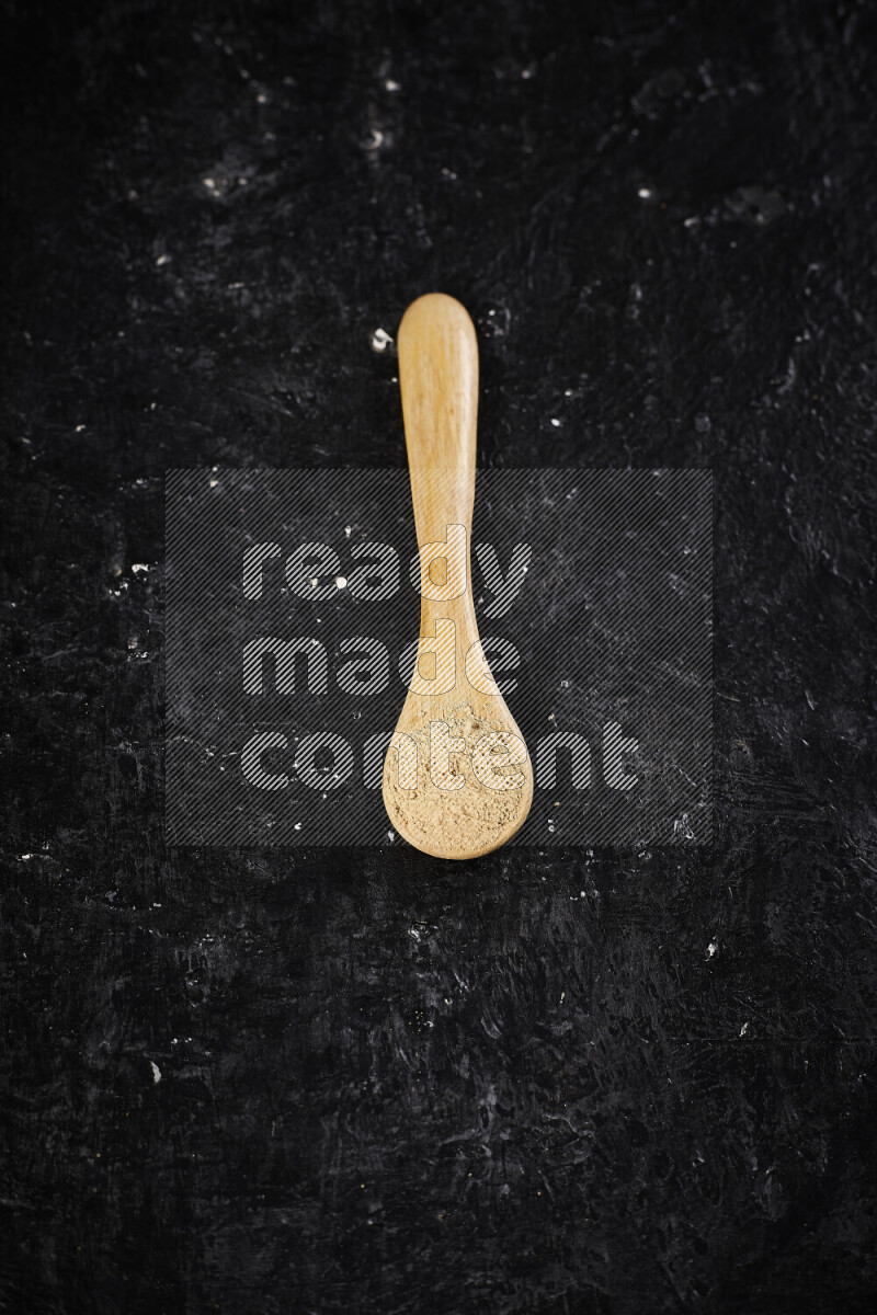 A wooden spoon full of ground ginger powder on black background