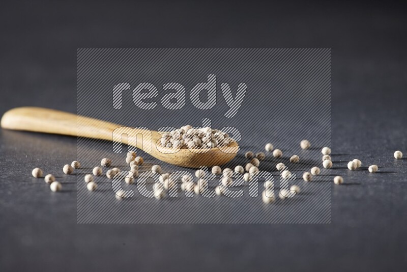 A wooden spoon full of white pepper beads on black flooring