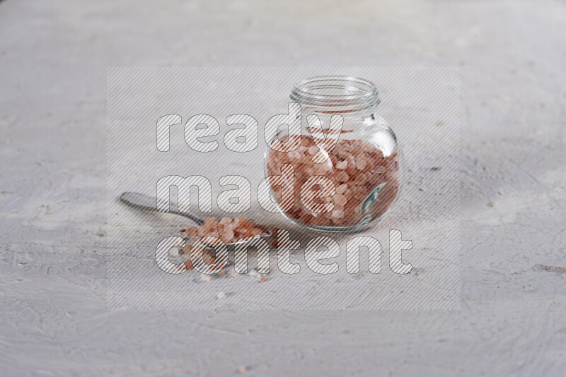 A glass jar full of coarse himalayan salt crystals on white background