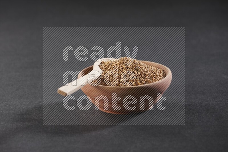 A wooden bowl and spoon full of mustard seeds on a black flooring