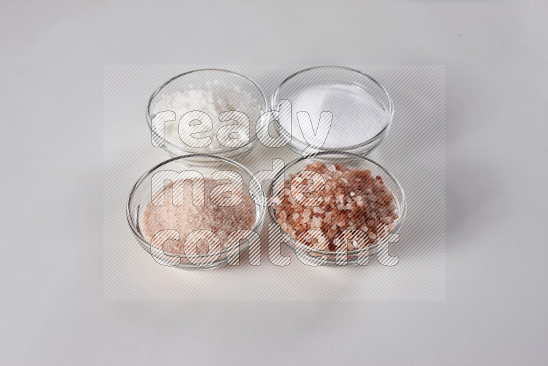 4 glass bowls filled with table salt, coarse sea salt, fine himalayan salt and coarse himalayan salt on white background