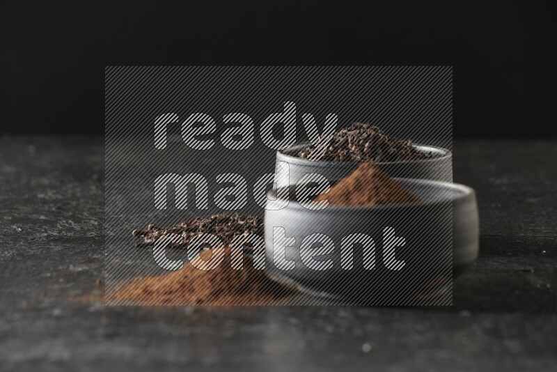 وعاءين من الفخار الأسود أحدهما ممتلئي بحبوب القرنفل والآخر ممتلئ ببودرة القرنفل على خلفية سوداء