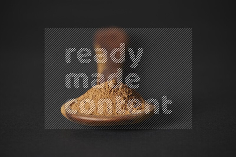 Cinnamon powder in a spoon ladle on black background