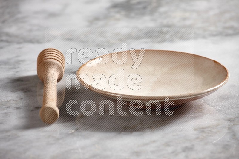 Beige Pottery Plate with wooden honey handle on the side with grey marble flooring, 15 degree angle
