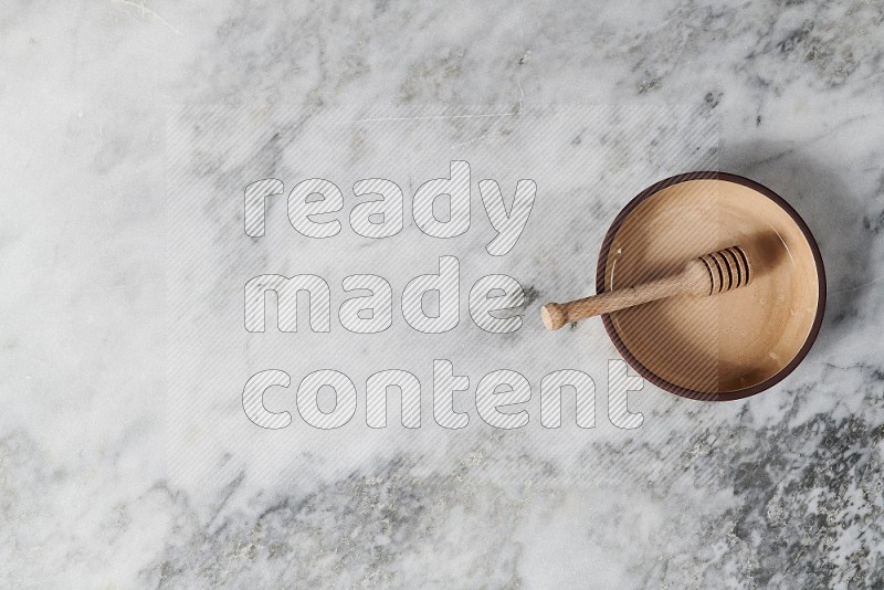 Beige Pottery Oven Plate with wooden honey handle in it, on grey marble flooring, Top View
