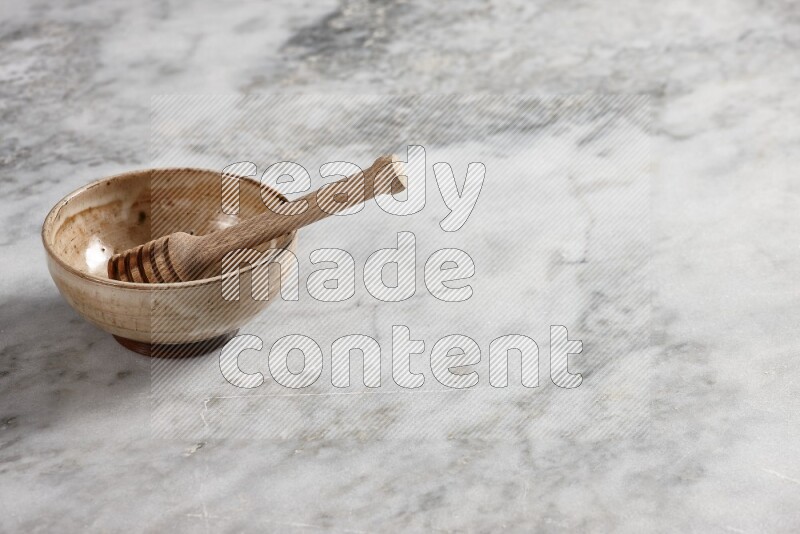 Beige pottery bowl with wooden honey dipper in it on grey marble background