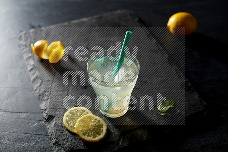 A glass of lemon juice with a straw on black background