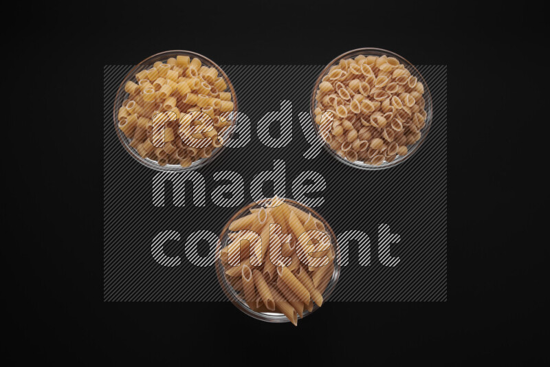 Different pasta types in glass bowls on black background