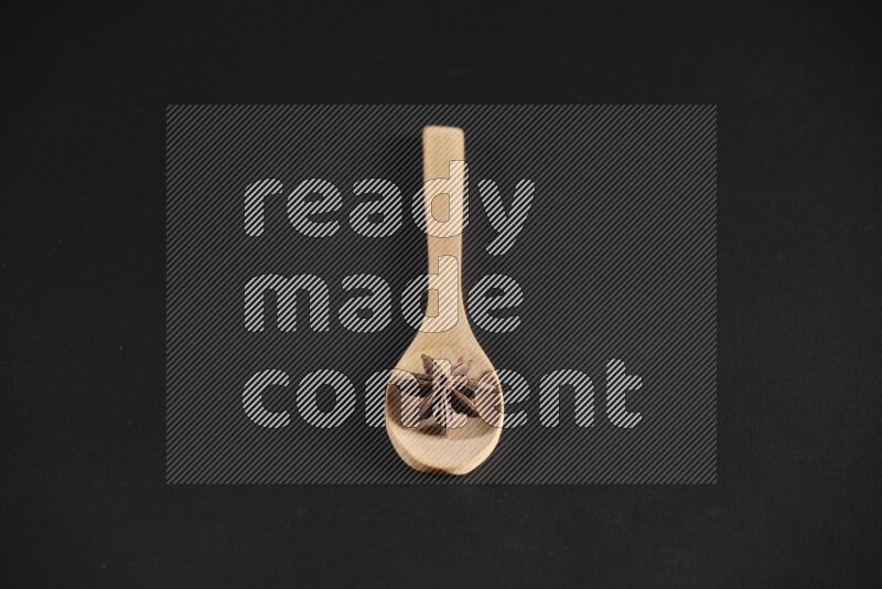 Star Anise in a wooden spoon on more stars anise filling the frame on black flooring