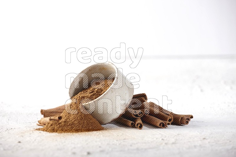 Ceramic beige bowl over filled with cinnamon powder and cinnamon sticks around the bowl on a textured white background in different angles
