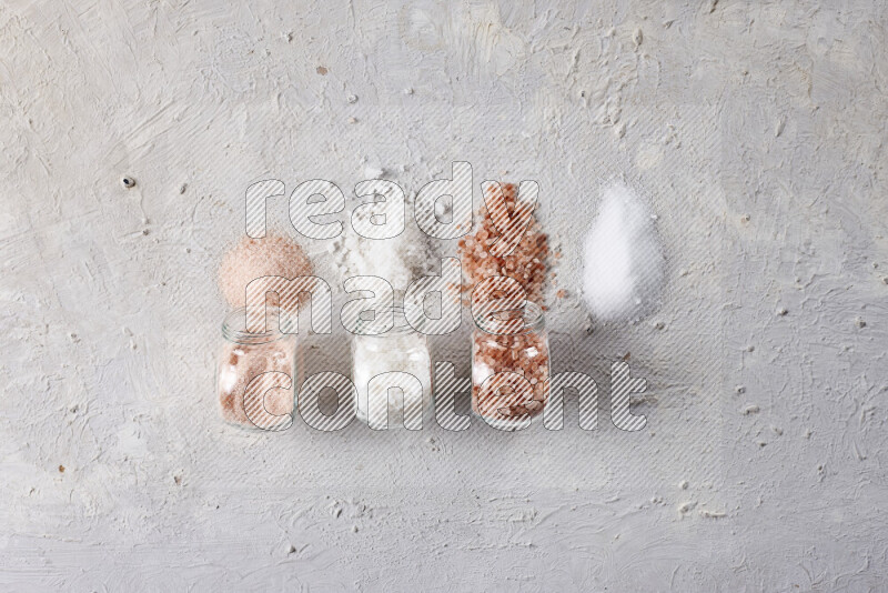 4 glass jars filled with table salt, coarse sea salt, fine himalayan salt and coarse himalayan salt on white background