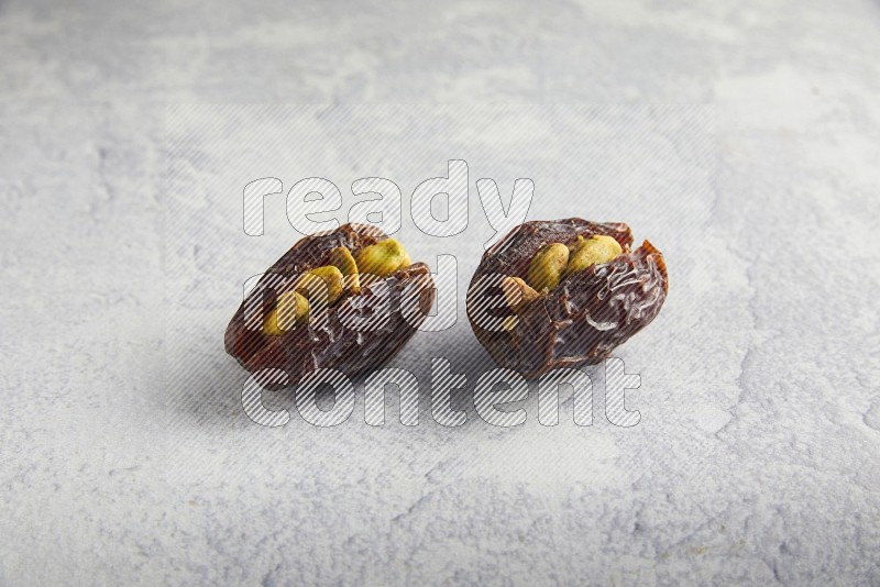 two pistachio stuffed madjoul date on a light grey background
