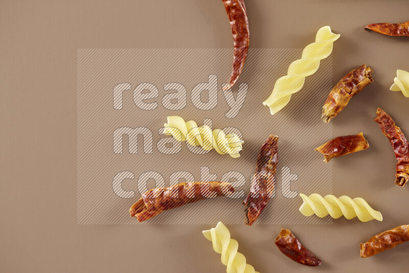 Raw pasta with different ingredients such as cherry tomatoes, garlic, onions, red chilis, black pepper, white pepper, bay laurel leaves, rosemary and cardamom on beige background