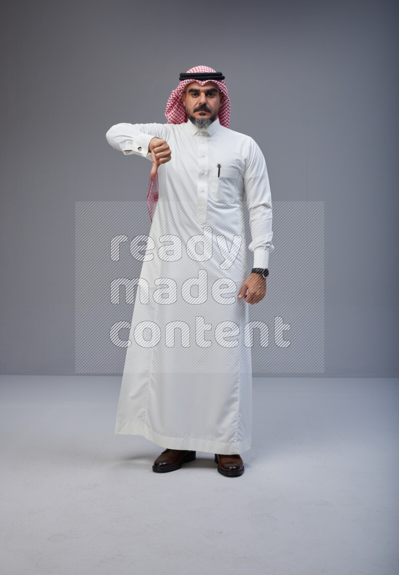 Saudi man Wearing Thob and red white Shomag standing interacting with the camera on Gray background