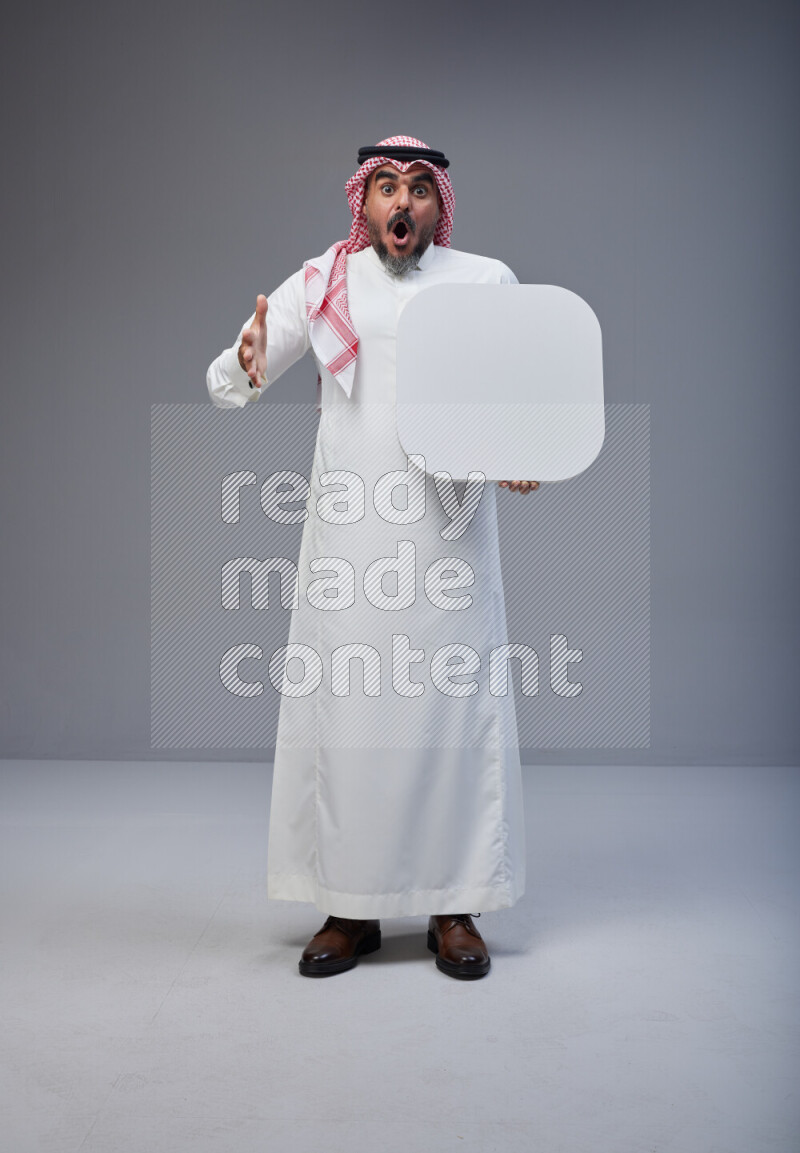 Saudi man Wearing Thob and red Shomag standing holding social media sign on Gray background