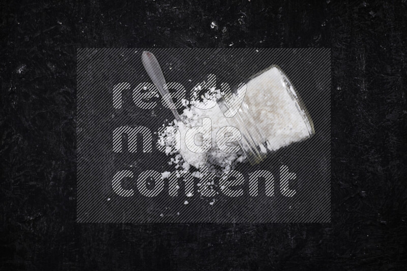 A glass jar full of coarse sea salt crystals on black background