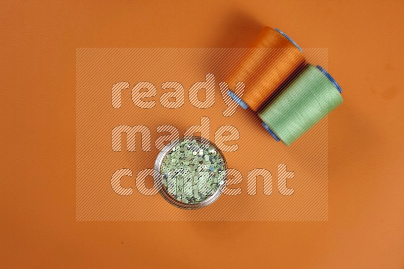 Green sewing supplies on orange background