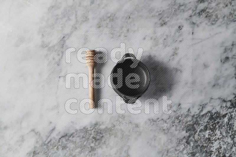 Black Pottery Bowl with wooden honey handle on the side on grey marble flooring, Top view