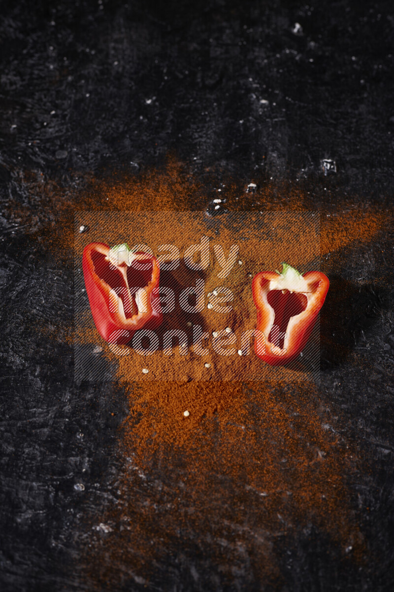 A bunch of ground paprika powder with two halfs of red bell pepper on black background