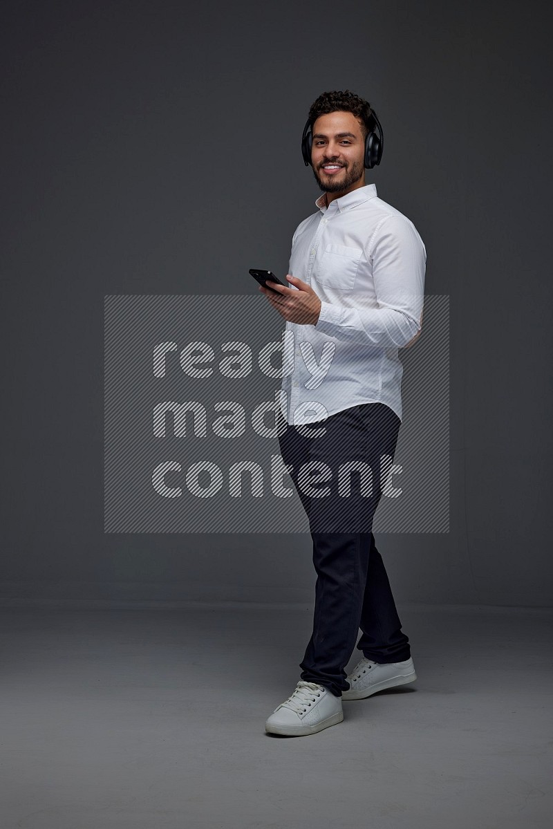 A man wearing smart casual and using his phone and headphone eye level on a gray background
