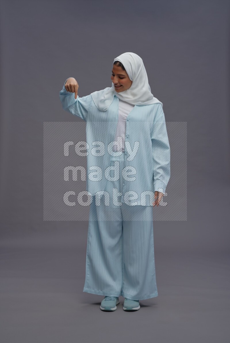 Saudi woman wearing hijab clothes standing interacting with the camera on gray background